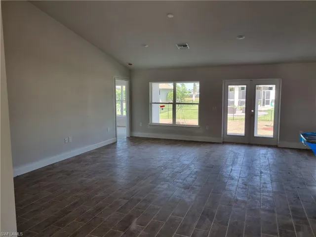 Unfurnished room featuring dark wood-type flooring, visible vents, baseboards, vaulted ceiling, and french doors