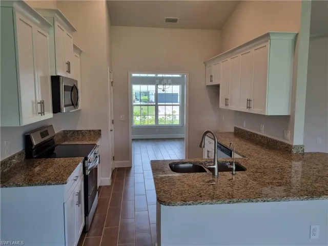 Kitchen with appliances with stainless steel finishes, a sink, dark stone countertops, a peninsula, and baseboards
