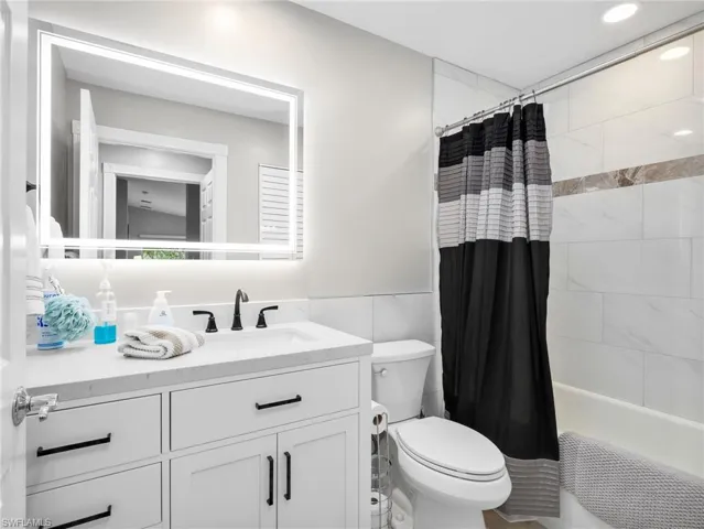 Full bath featuring vanity, shower / tub combo, and tile walls