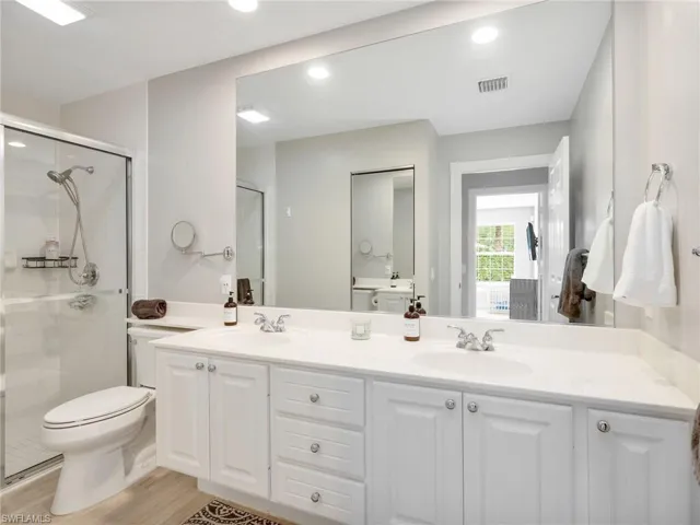 Full bath featuring double vanity, a shower stall, light wood-style flooring, and recessed lighting