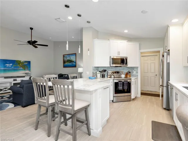 Kitchen featuring a breakfast bar area, open floor plan, stainless steel appliances, a peninsula, and white cabinetry