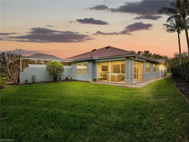 Back of house at dusk featuring a tiled roof, stucco siding, a sunroom, and a lawn