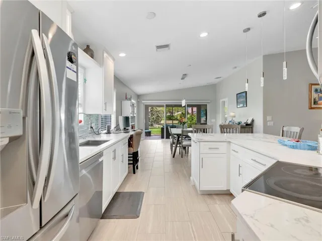 Kitchen featuring stainless steel appliances, lofted ceiling, white cabinetry, and hanging light fixtures