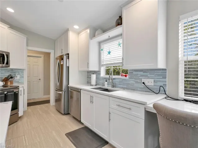 Kitchen featuring white cabinetry, stainless steel appliances, backsplash, light stone countertops, and recessed lighting