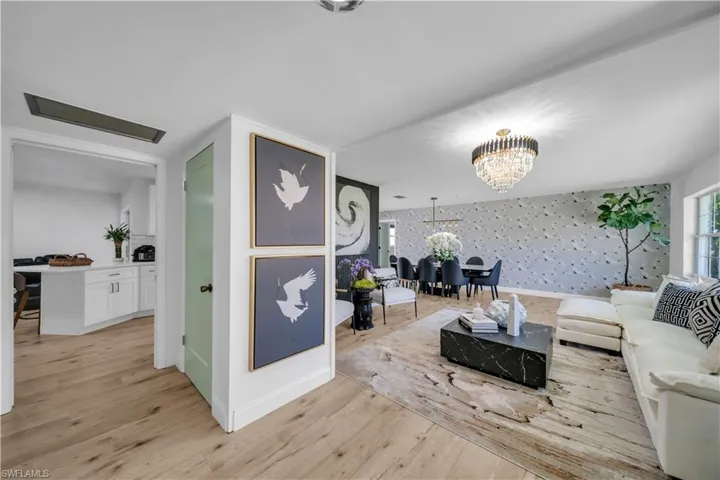 Living room featuring wallpapered walls, a chandelier, light wood-style flooring, and an accent wall