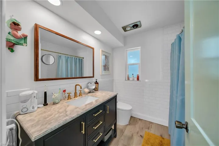 Bathroom with tile walls, vanity, wood finished floors, a wainscoted wall, and a shower with curtain