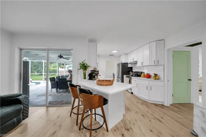 Kitchen with appliances with stainless steel finishes, a breakfast bar, white cabinets, light wood finished floors, and recessed lighting