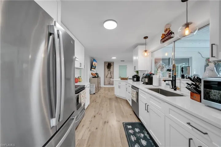 Kitchen with stainless steel appliances, white cabinetry, light countertops, decorative light fixtures, and light wood-type flooring