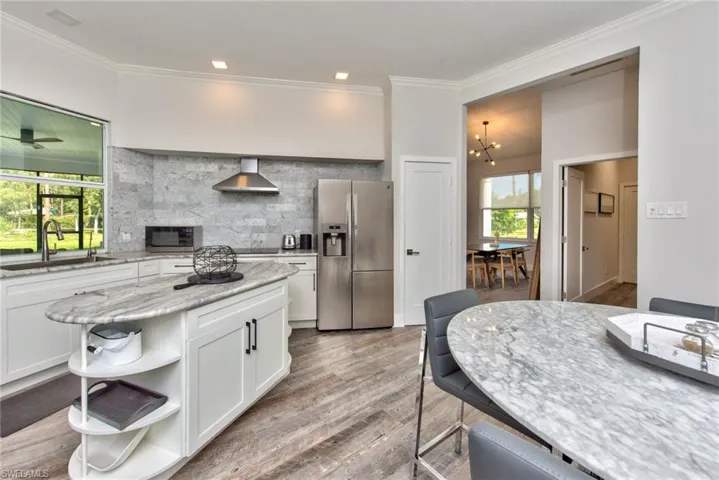 Kitchen with stainless steel appliances, wall chimney exhaust hood, sink, light stone countertops, and white cabinets