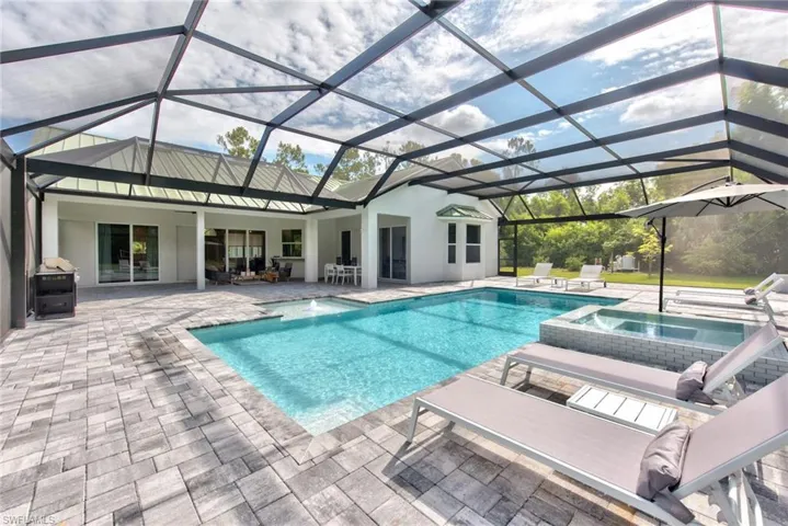 View of pool with an in ground hot tub, glass enclosure, and a patio