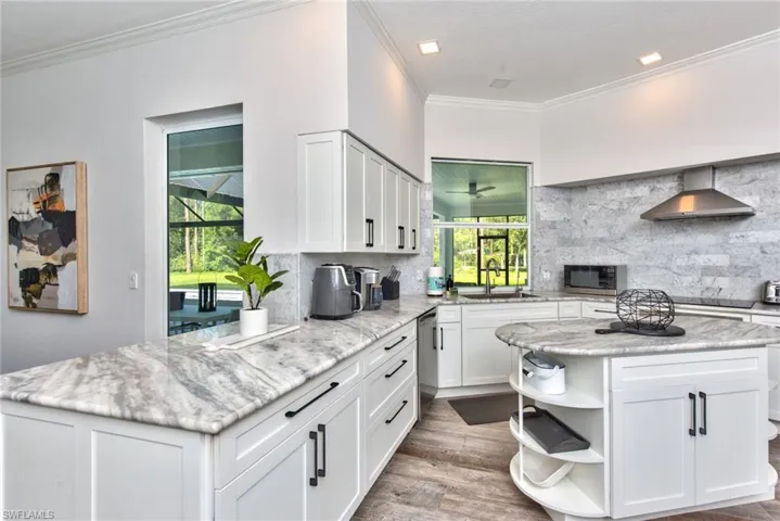 Kitchen featuring backsplash, sink, ornamental molding, appliances with stainless steel finishes, and wall chimney range hood