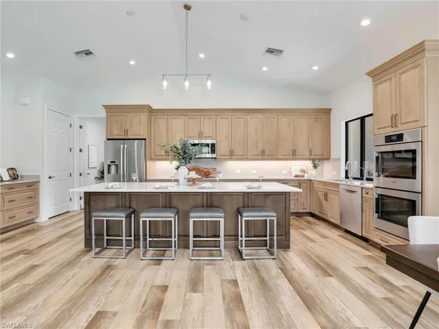 Kitchen featuring hanging light fixtures, LVP light wood-style flooring, light brown cabinets, a kitchen bar, and lofted ceiling
