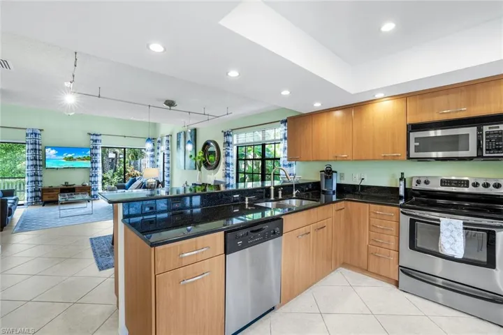 Kitchen featuring stainless steel appliances, open floor plan, brown cabinets, dark stone counters, and recessed lighting