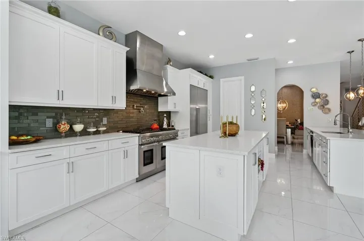Kitchen with white cabinets, wall chimney range hood, a large island, high end appliances, and tasteful backsplash