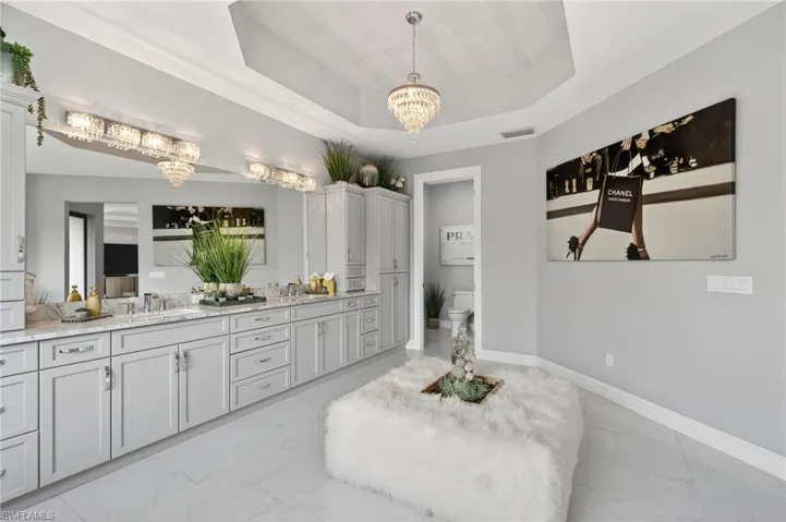 Bathroom with double vanity, a tray ceiling, a chandelier, and light marble finish floors