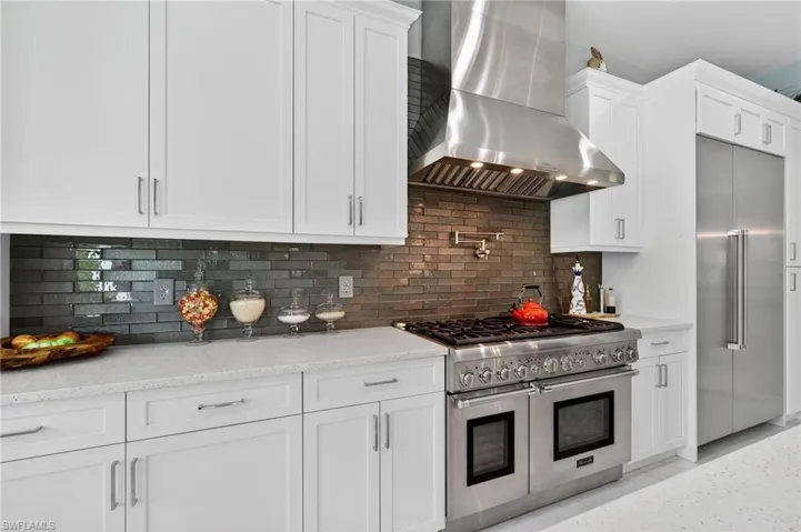 Kitchen featuring wall chimney exhaust hood, high end appliances, decorative backsplash, and white cabinets