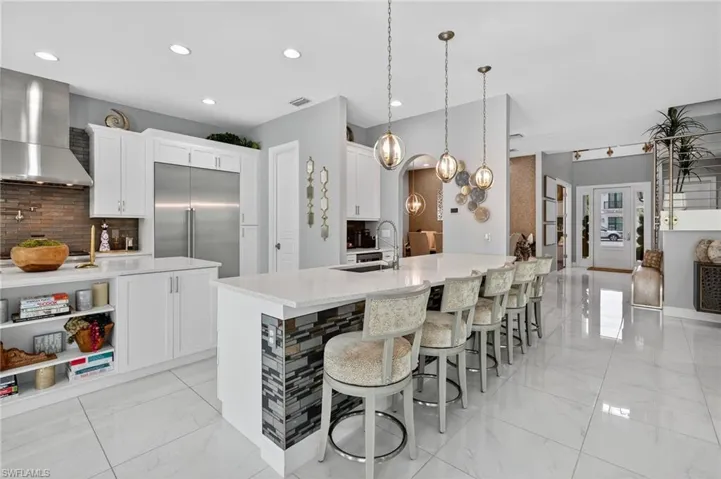 Kitchen featuring backsplash, white cabinetry, light marble finish flooring, wall chimney range hood, and recessed lighting