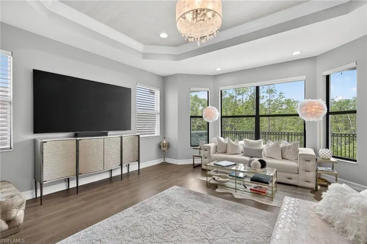 Living area with wood finished floors, a raised ceiling, crown molding, a chandelier, and recessed lighting