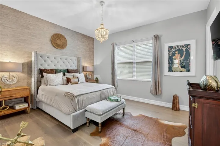 Bedroom with light wood finished floors, an accent wall, and a chandelier