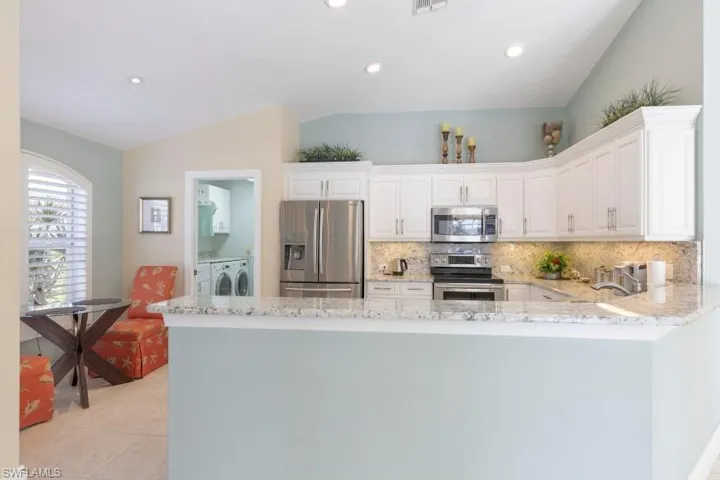 Kitchen featuring kitchen peninsula, appliances with stainless steel finishes, white cabinets, washing machine and dryer, and lofted ceiling