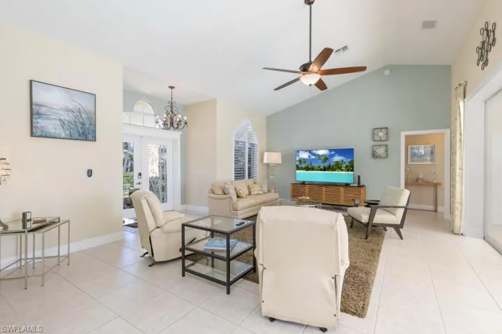 Tiled living room featuring ceiling fan with notable chandelier, high vaulted ceiling, and french doors