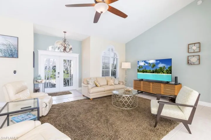 Living room with ceiling fan with notable chandelier, light tile patterned flooring, high vaulted ceiling, and french doors
