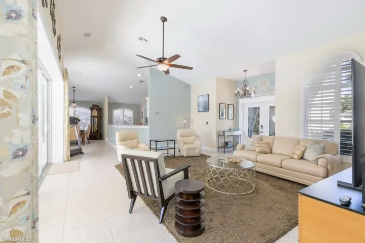 Living room with a towering ceiling, ceiling fan with notable chandelier, and light tile patterned flooring