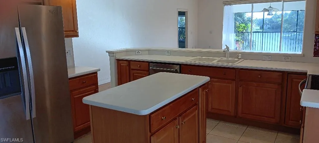 Kitchen featuring light tile patterned flooring, sink, a kitchen island, dishwasher, and stainless steel fridge
