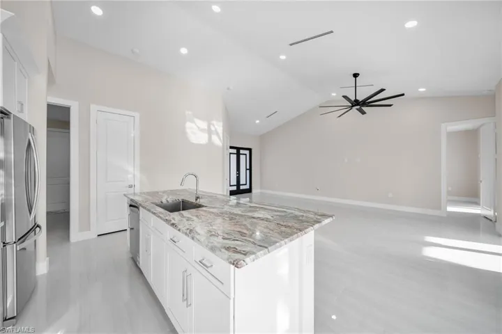 Kitchen featuring white cabinets, light stone counters, appliances with stainless steel finishes, lofted ceiling, and recessed lighting