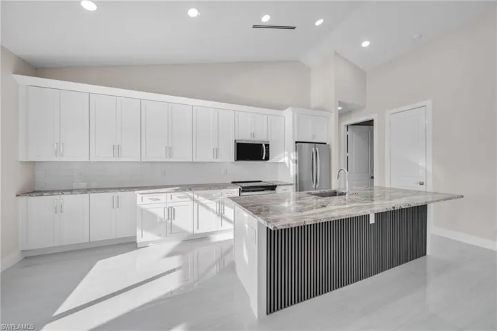 Kitchen featuring decorative backsplash, appliances with stainless steel finishes, an island with sink, light stone counters, and white cabinets