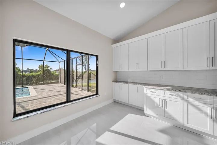 Kitchen with lofted ceiling, white cabinetry, light stone counters, decorative backsplash, and a sunroom
