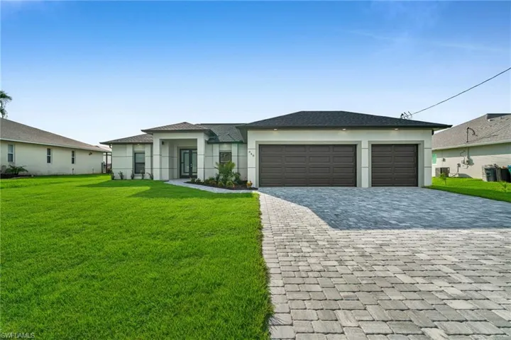Prairie-style home with a front lawn, decorative driveway, an attached garage, and stucco siding