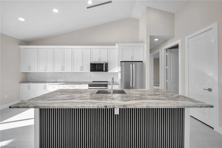 Kitchen with appliances with stainless steel finishes, lofted ceiling, light stone countertops, white cabinets, and decorative backsplash