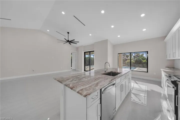 Kitchen with white cabinets, stainless steel appliances, a kitchen island with sink, light stone countertops, and recessed lighting