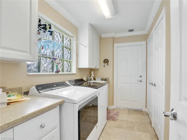 Laundry area featuring ornamental molding, washer and dryer, cabinets, and light tile floors