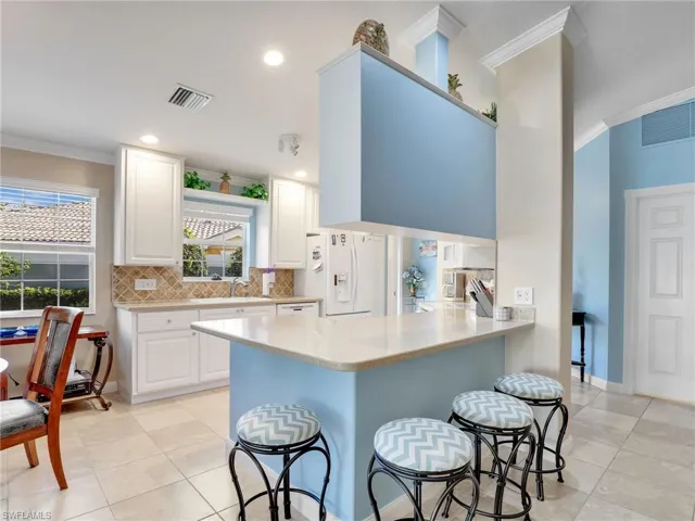 Kitchen featuring backsplash, a kitchen bar, white appliances, and light tile floors