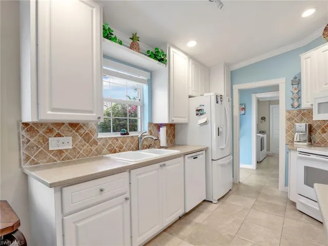 Kitchen with white appliances, sink, white cabinetry, and tasteful backsplash