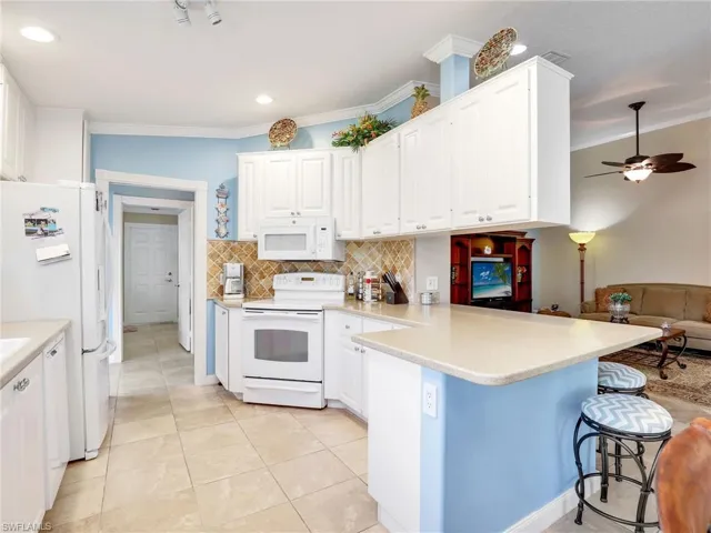 Kitchen with white appliances, a breakfast bar area, kitchen peninsula, backsplash, and ceiling fan