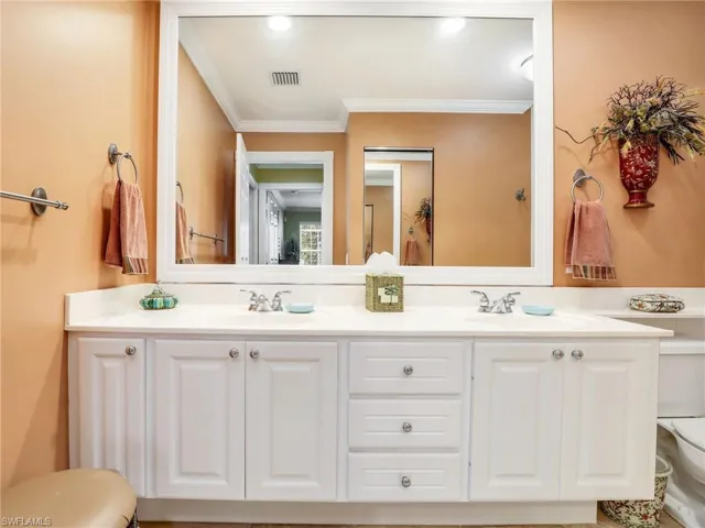 Bathroom with ornamental molding, double sink, oversized vanity, and toilet