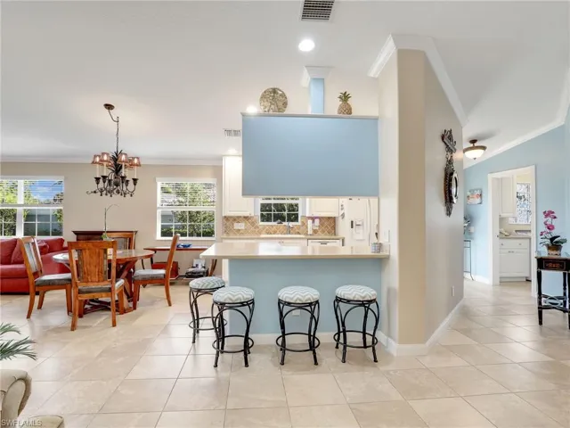 Kitchen featuring light tile flooring, tasteful backsplash, crown molding, a kitchen bar, and white cabinetry