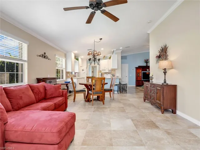 Tiled living room featuring ceiling fan with notable chandelier and crown molding