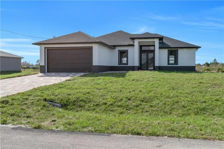 Prairie-style home featuring stucco siding, decorative driveway, roof with shingles, and a front lawn