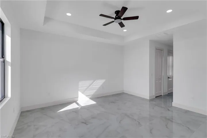 Unfurnished room with a tray ceiling, ceiling fan, recessed lighting, and light marble finish floors