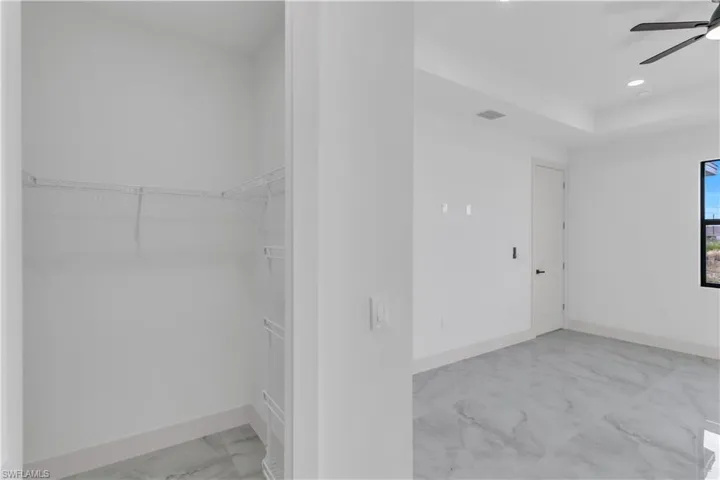Walk in closet with light marble finish floors and ceiling fan
