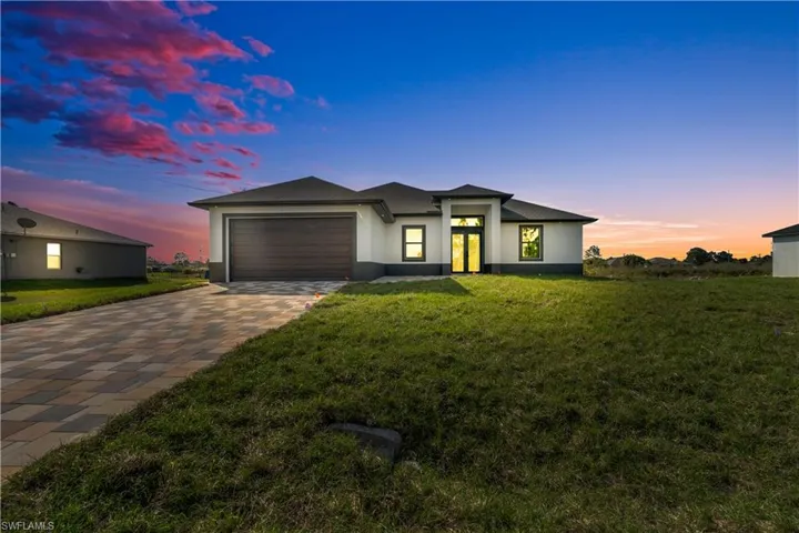 Prairie-style home featuring a lawn, a garage, stucco siding, and driveway