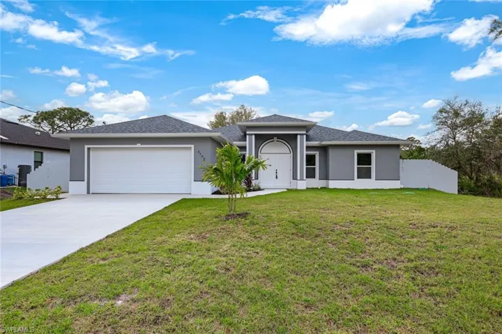 View of front of property featuring a garage, concrete driveway, a front lawn, and fence