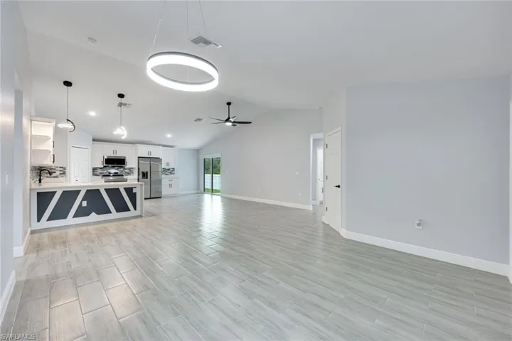 Unfurnished living room with visible vents, a ceiling fan, light wood-style flooring, vaulted ceiling, and a sink
