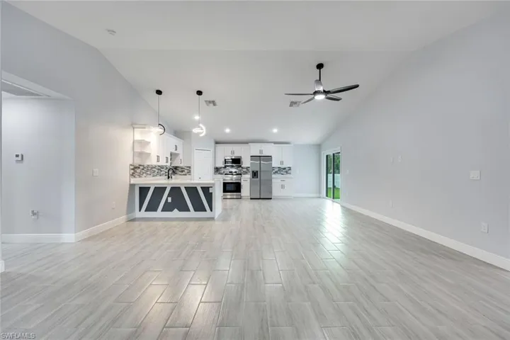 Unfurnished living room featuring visible vents, light wood-style flooring, a ceiling fan, a sink, and baseboards