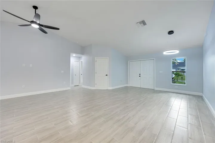 Unfurnished living room featuring light wood finished floors, baseboards, visible vents, a ceiling fan, and lofted ceiling