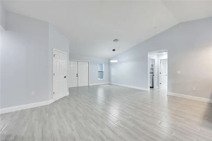 Unfurnished living room with light wood-style floors, visible vents, vaulted ceiling, and baseboards